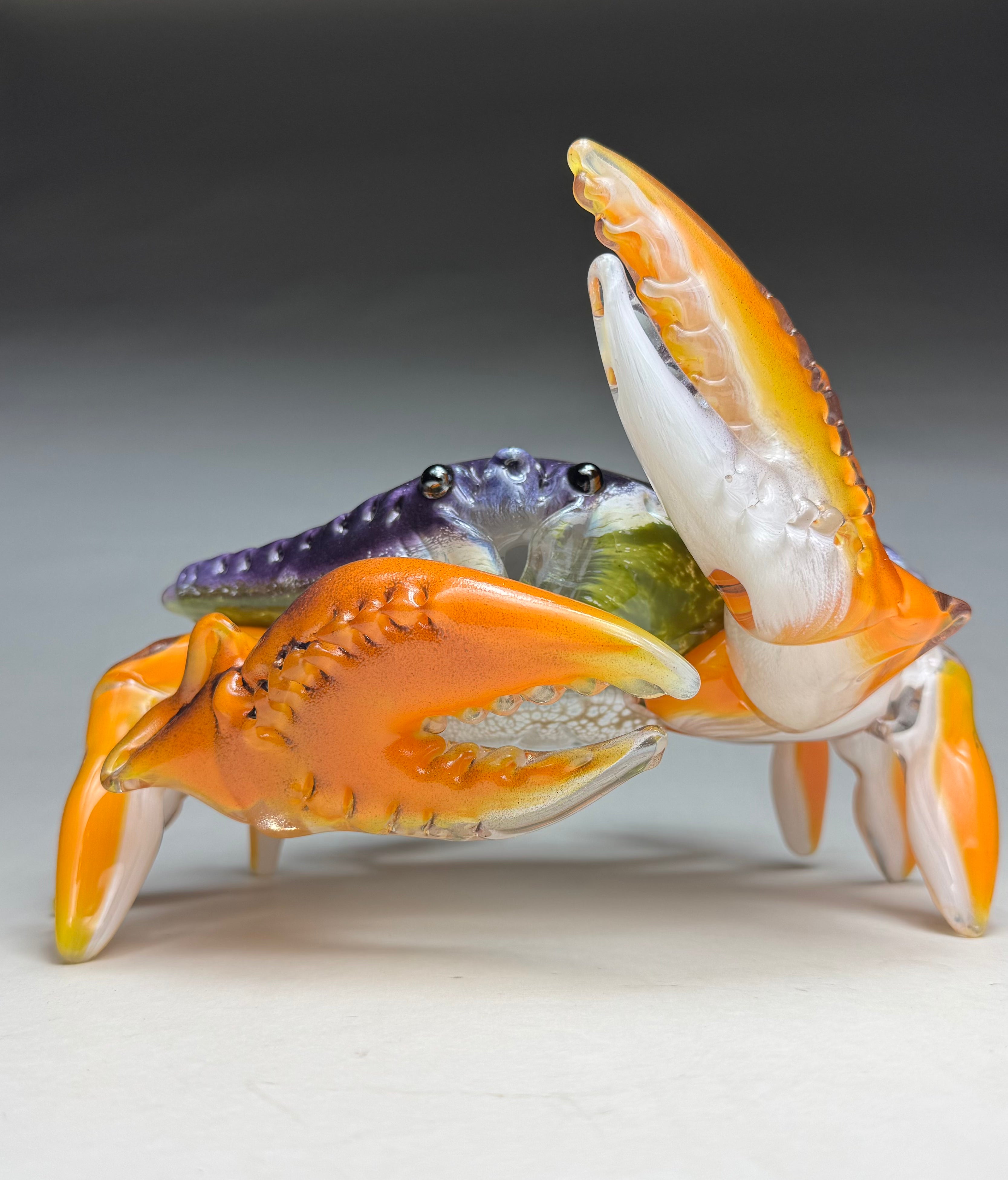 Glass crab figurine with orange, white, and purple colors on a gray background